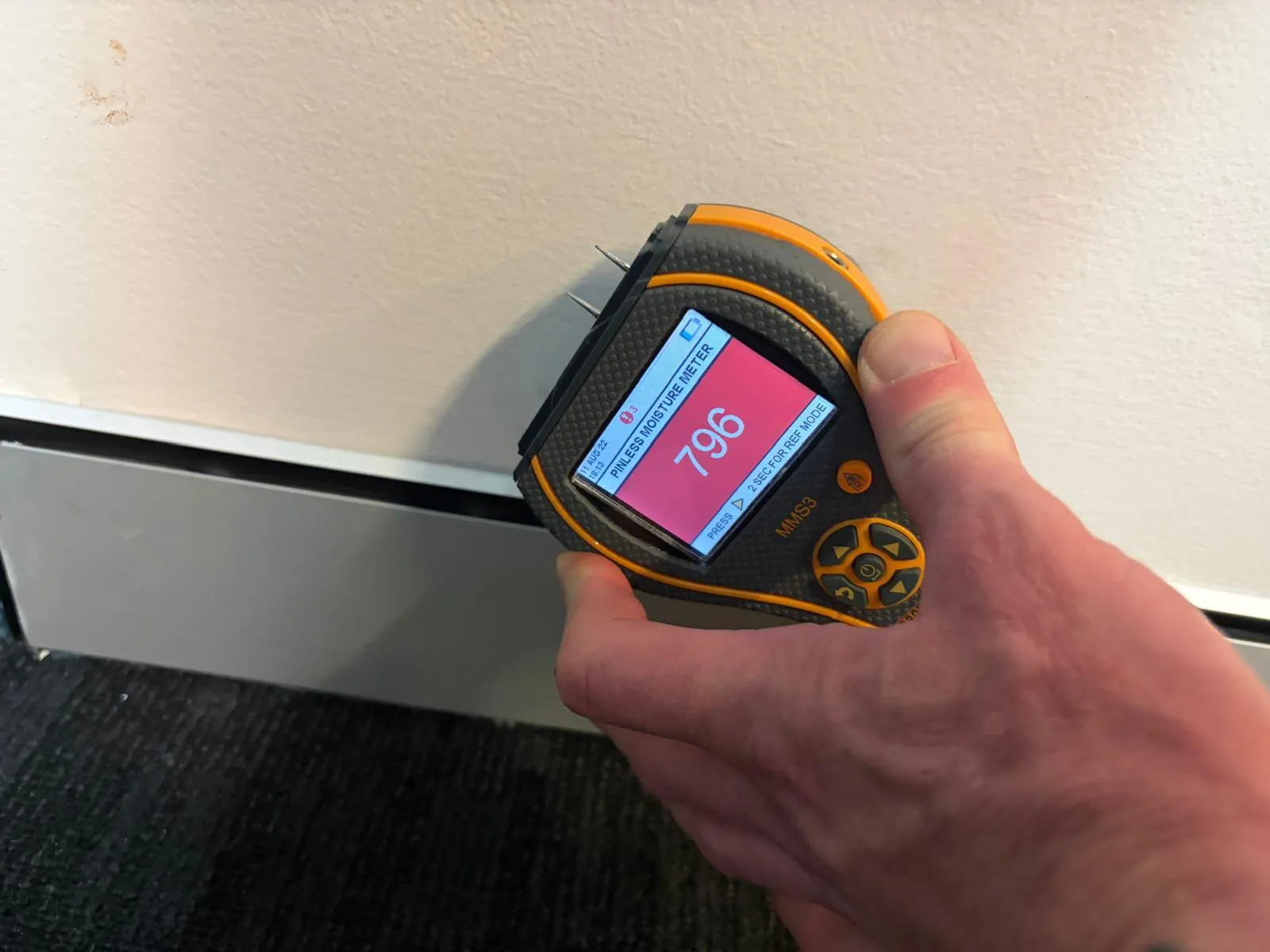 Technician taking a moisture reading at an interior wall